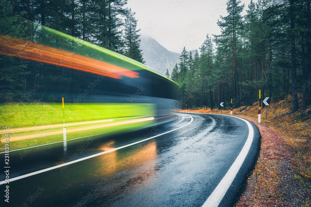 Blurred green bus on the road in autumn forest in rain. Perfect asphalt mountain road in overcast ra