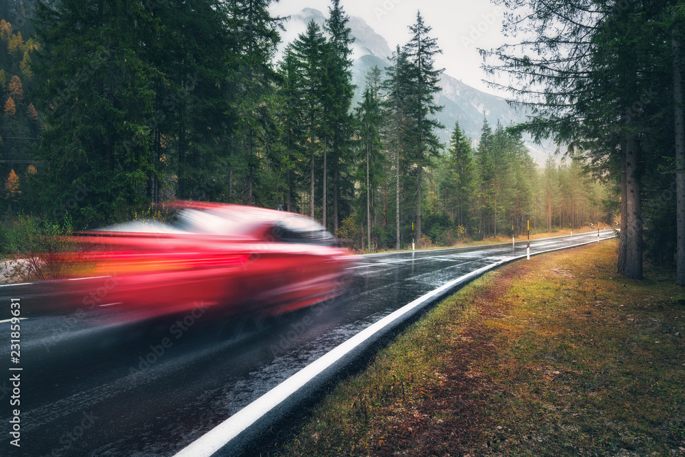 Blurred red car in motion on the road in autumn forest in rain. Perfect asphalt mountain road in ove