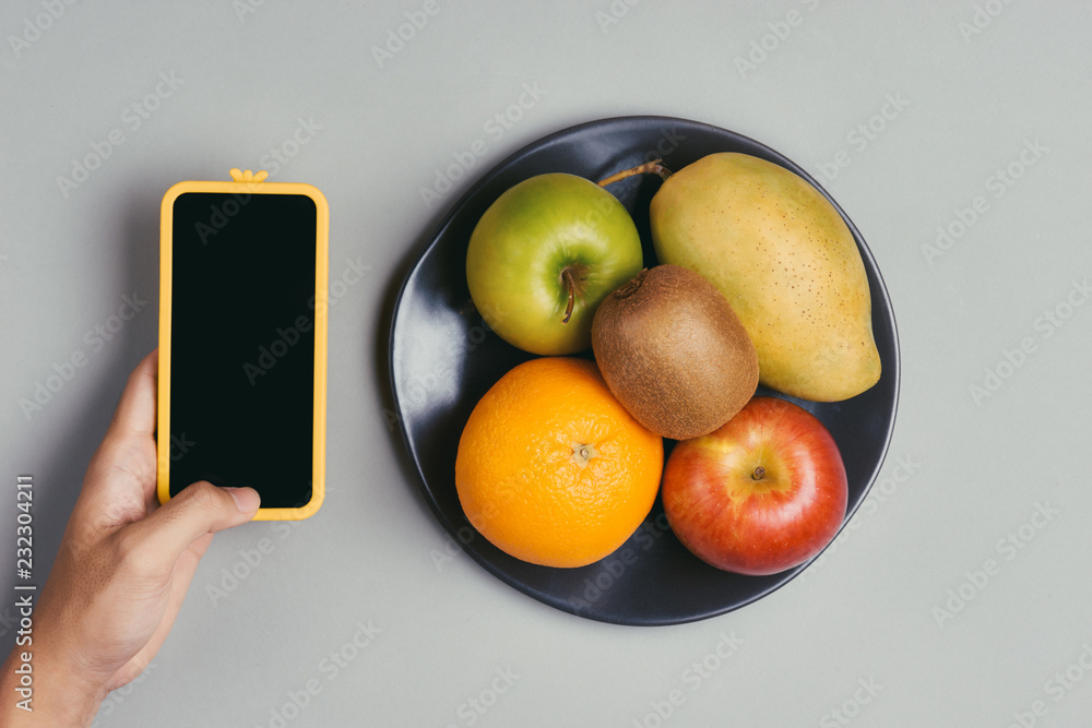 Male hand holding a smartphone against fresh fruits