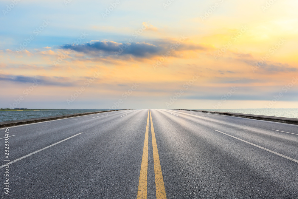 Asphalt road and dramatic sky with coastline at sunset