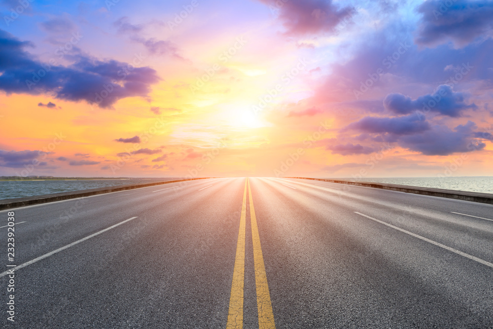 Asphalt road and dramatic sky with coastline at sunset