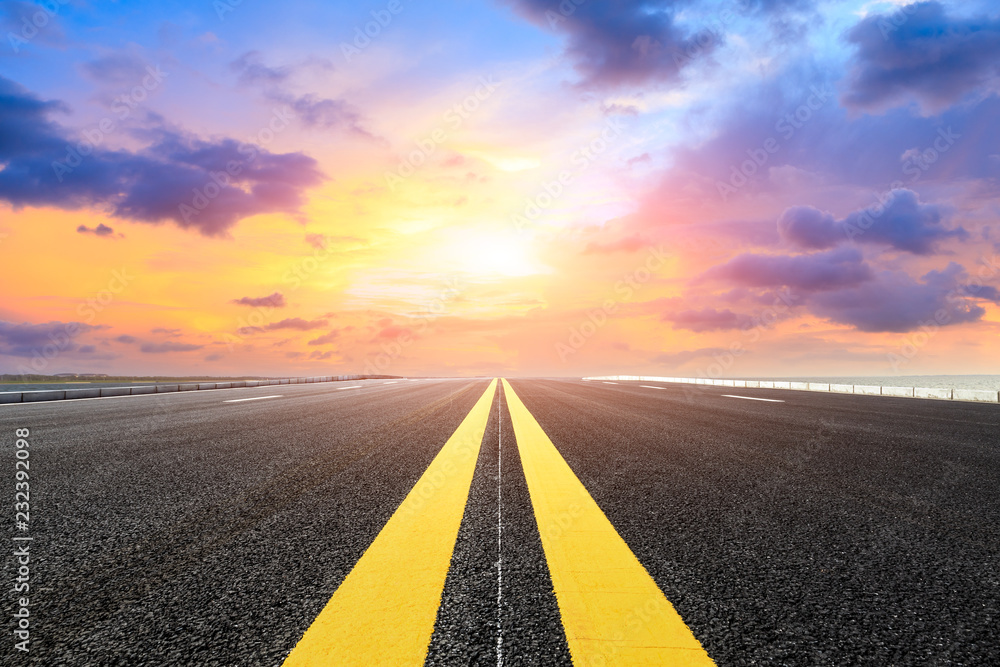 Asphalt road and dramatic sky with coastline at sunset