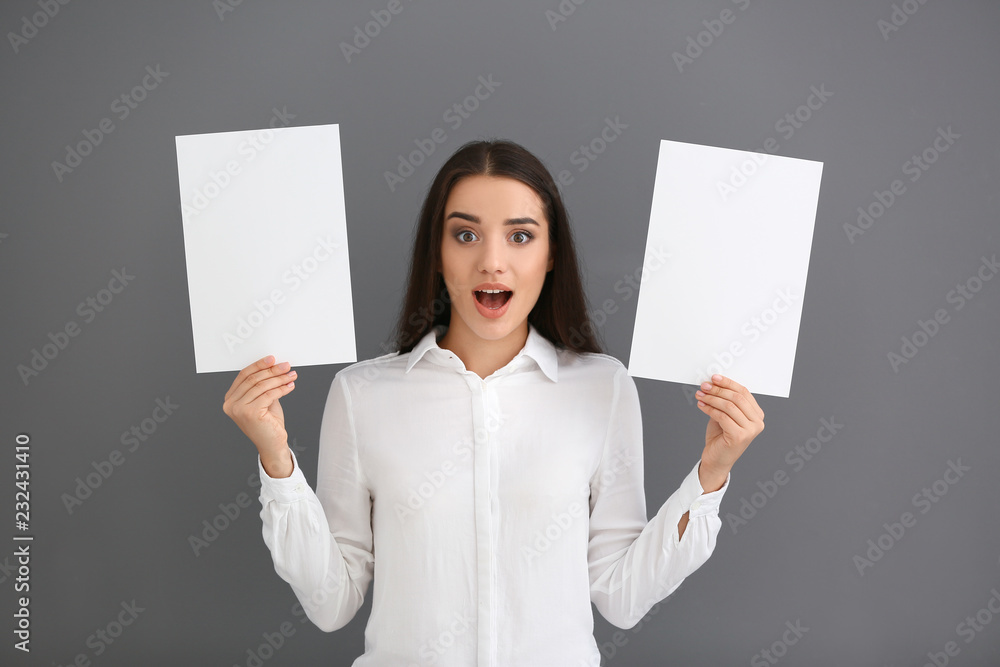 Emotional young woman with blank sheets of paper on grey background