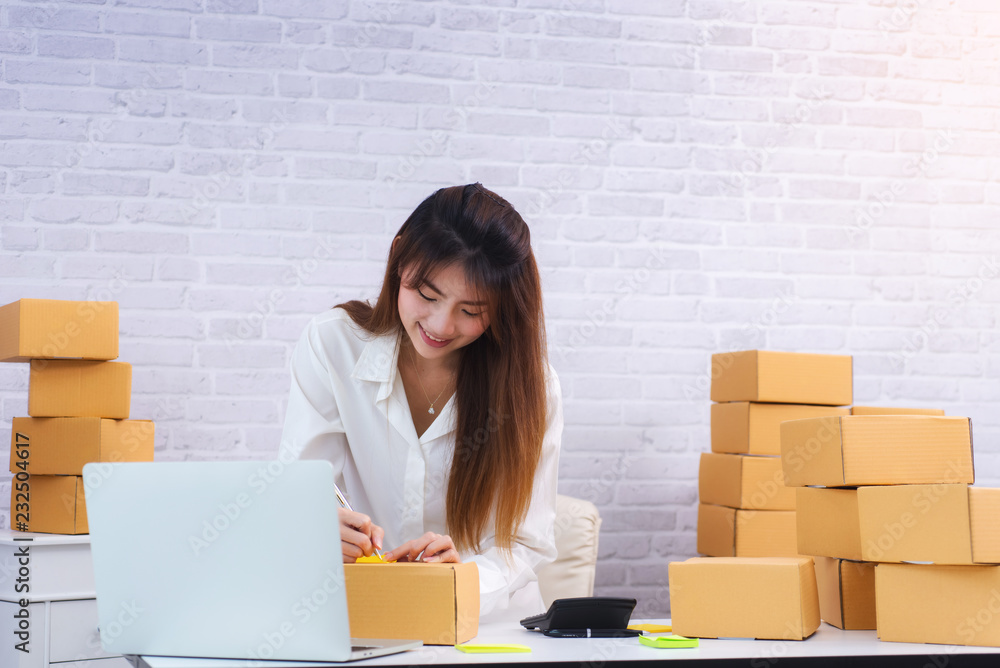 Women business owner writing address on packing box at workplace in home offce. online shopping SME 