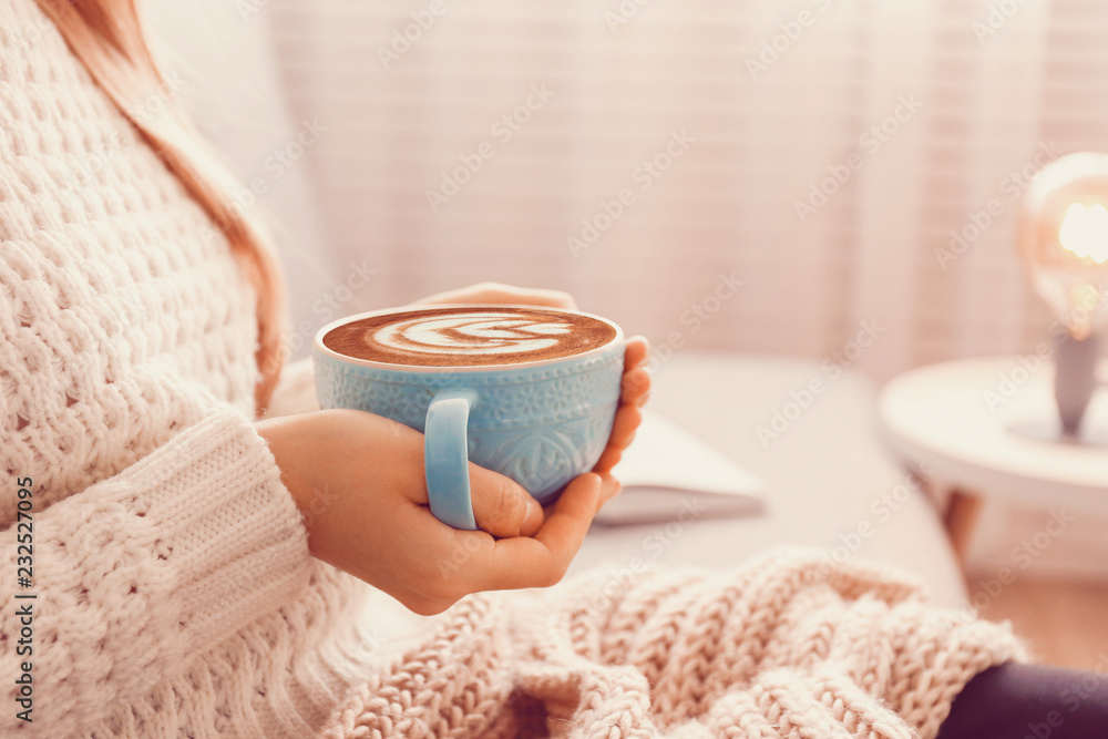 Close up young womans hands holding big cup of hot beverage. Female wearing fashionable oversized w