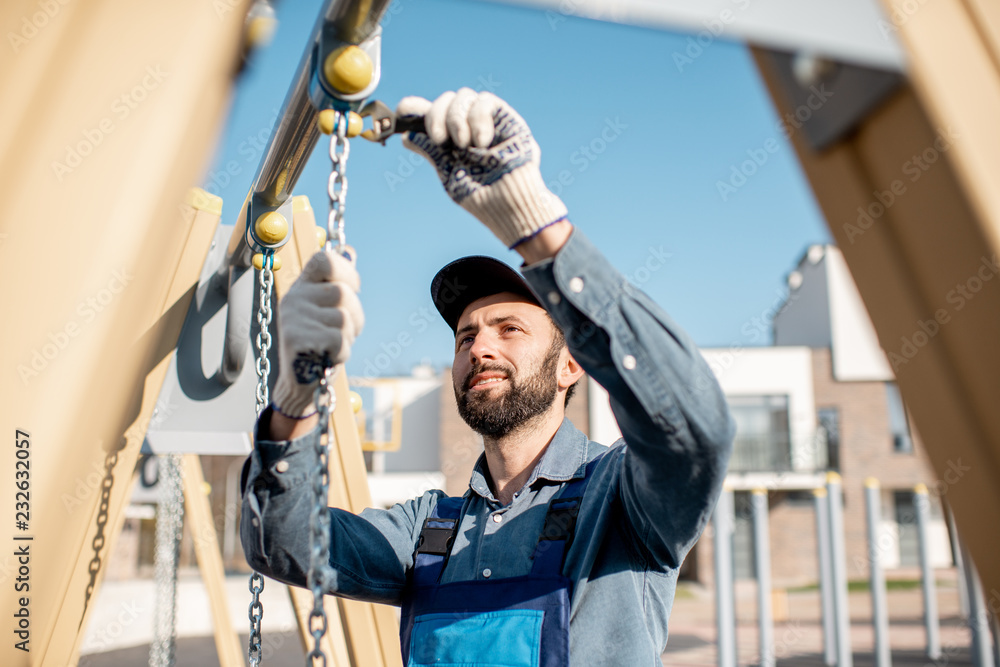 穿着制服的英俊工人在户外操场上安装秋千