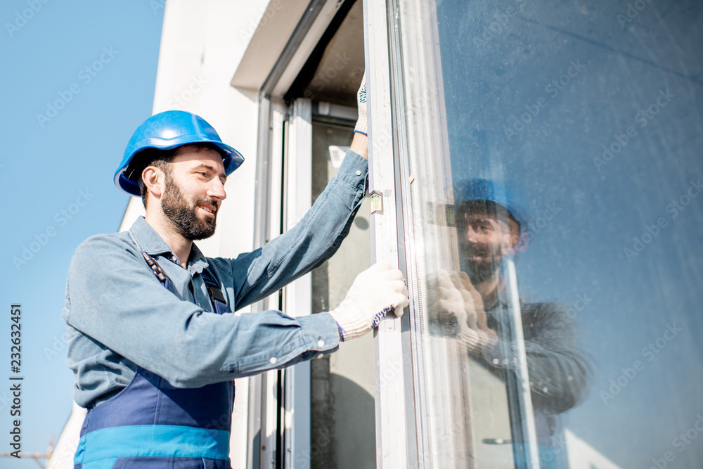 Workman in uniform mounting windows checking the level on the white building facade