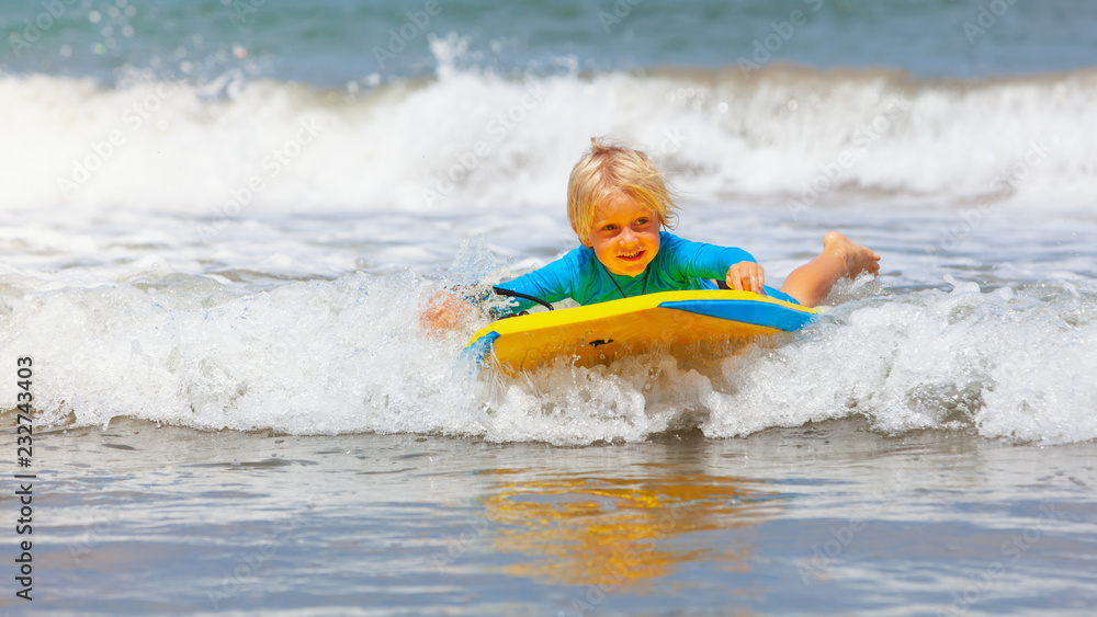 Happy baby boy - young surfer ride on surfboard with fun on sea waves. Active family lifestyle, kids