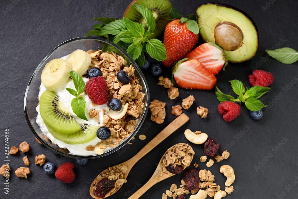 Yogurt with granola and fruits in glass on black granite stone table