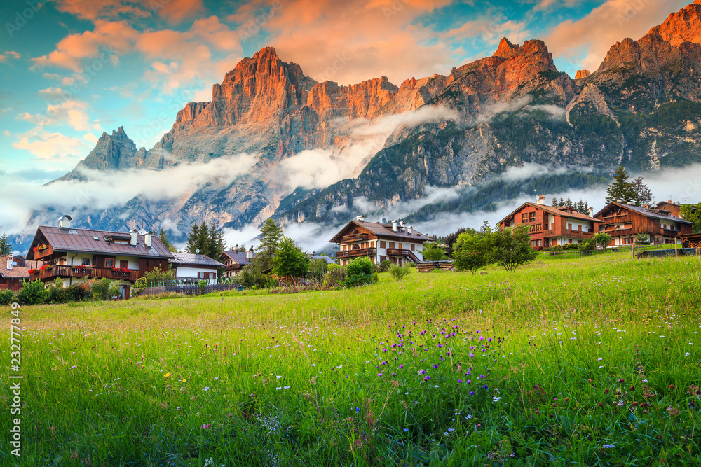 Spring alpine landscape with flowers, mountains and wooden houses, Italy