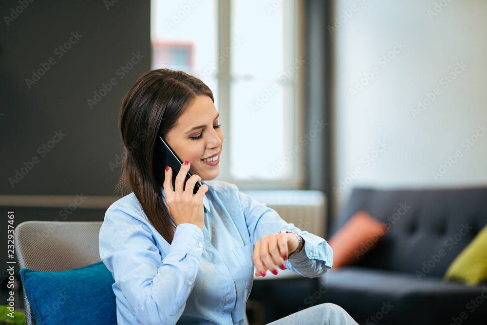 Young businesswoman checking the time and talking on the phone indoors.