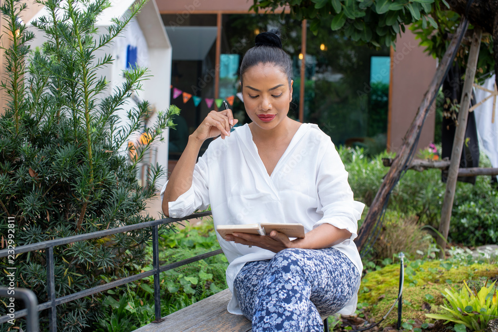 Portrait of a beautiful woman writing in a book are sitting thinking about the job at the park,Relax