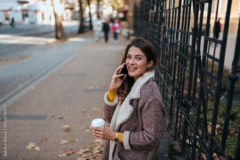 Young woman in the street drinking coffee and talking on the phone.