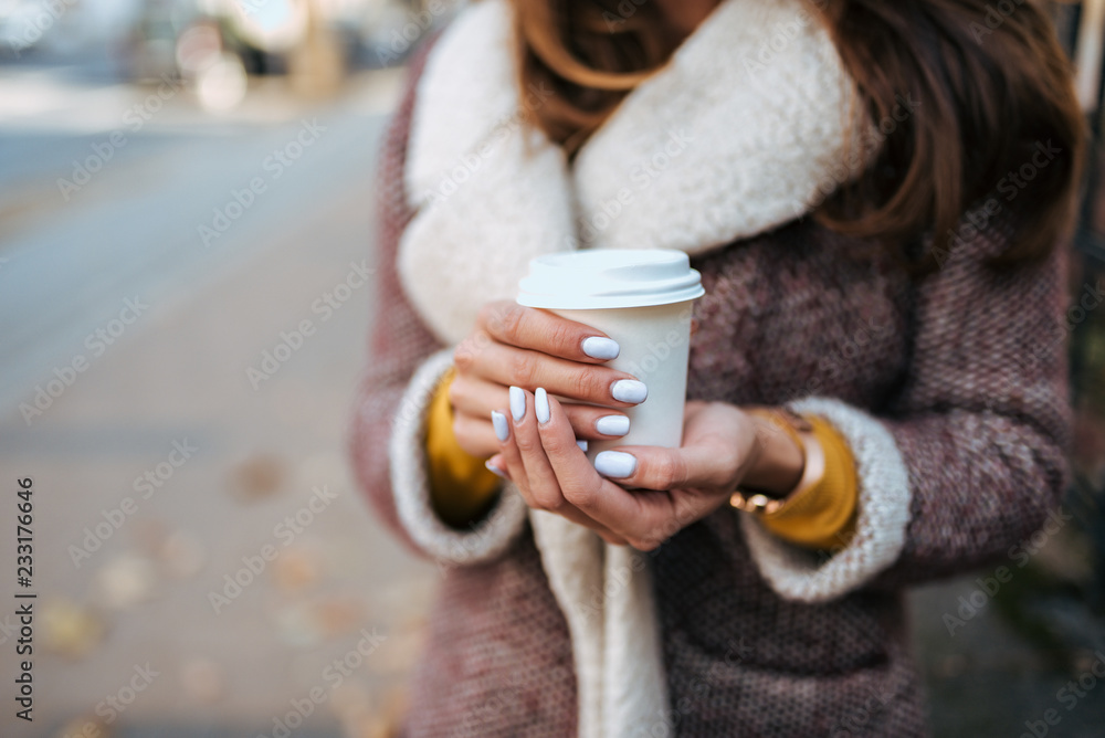 Close-up image of young woman holding take away coffee cup outdoors.