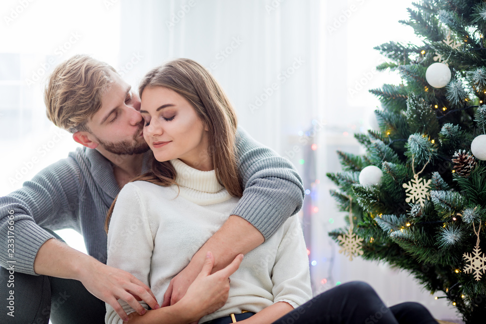 Couple celebrating Christmas together, sitting on floor next to Xmas tree