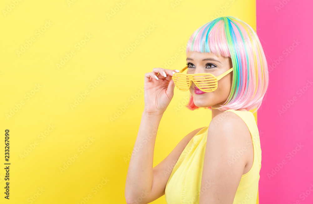 Young woman in a colorful wig with shutter shades sunglasses on a split yellow and pink background