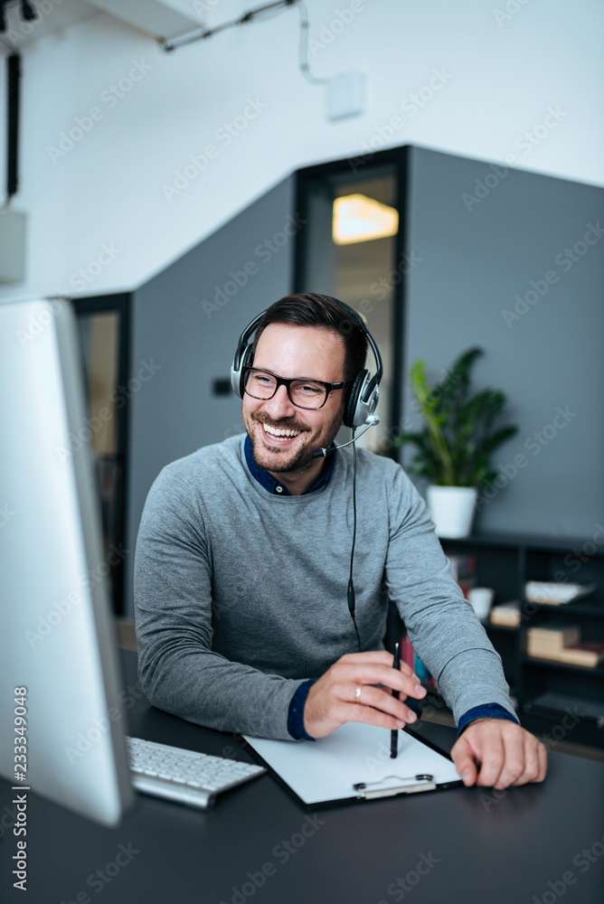 Happy handsome tech manager talking with client on headset.