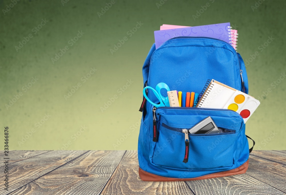 Open blue school backpack on wooden desk and gray background.