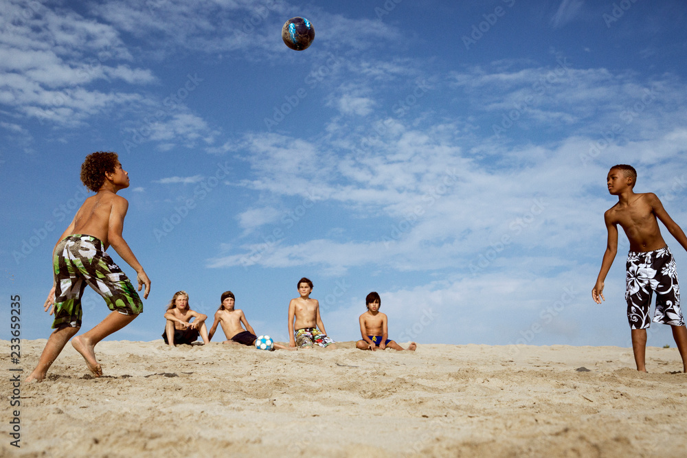 Boys looking at friends playing soccer against sky