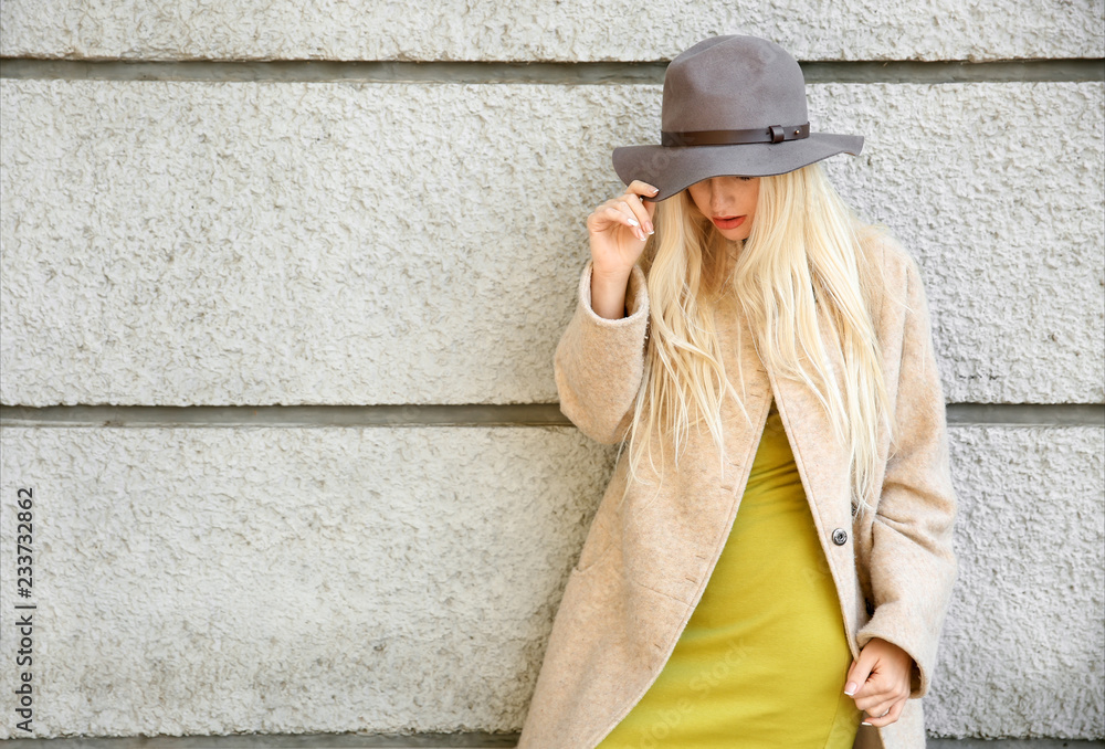 Beautiful fashionable woman near light wall