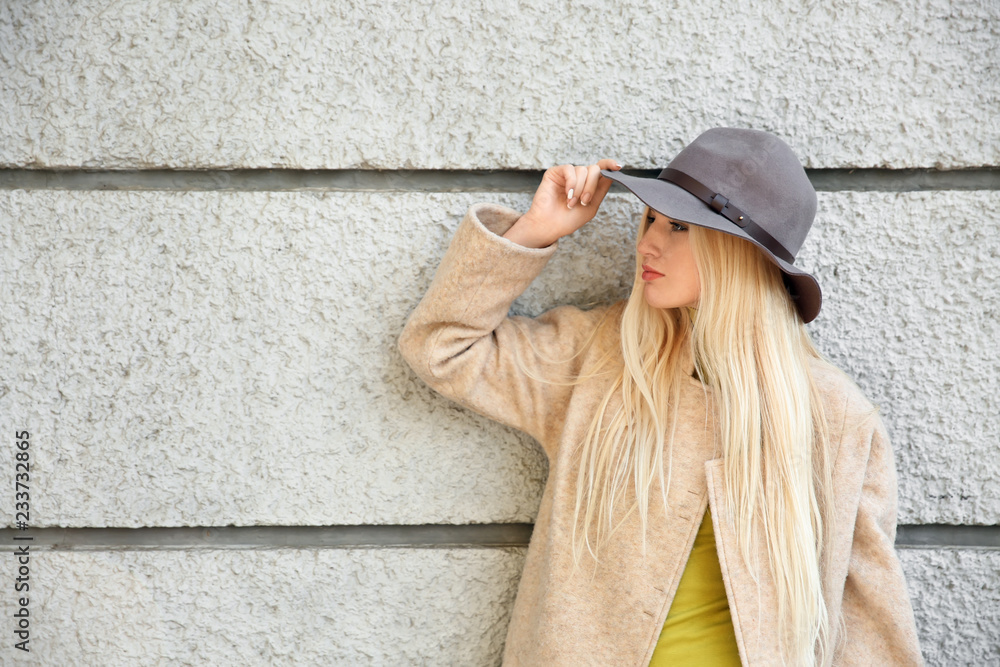 Beautiful fashionable woman near light wall