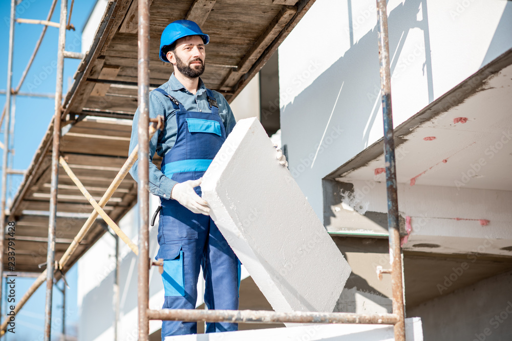 建筑工人用站在建筑脚手架上的泡沫板温暖建筑立面