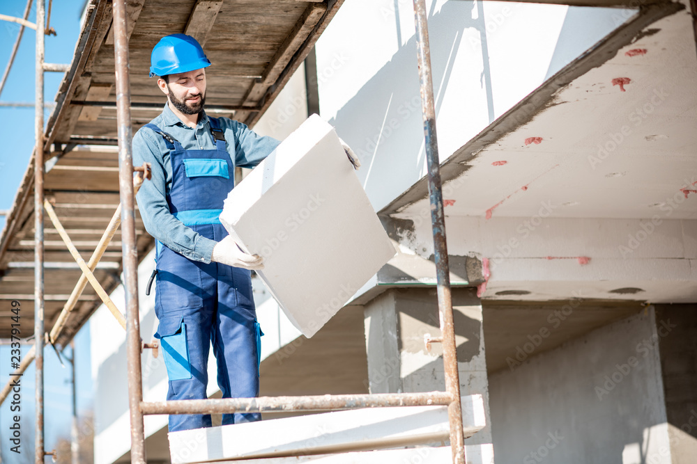 建筑工人用建筑脚手架上的泡沫板温暖建筑立面