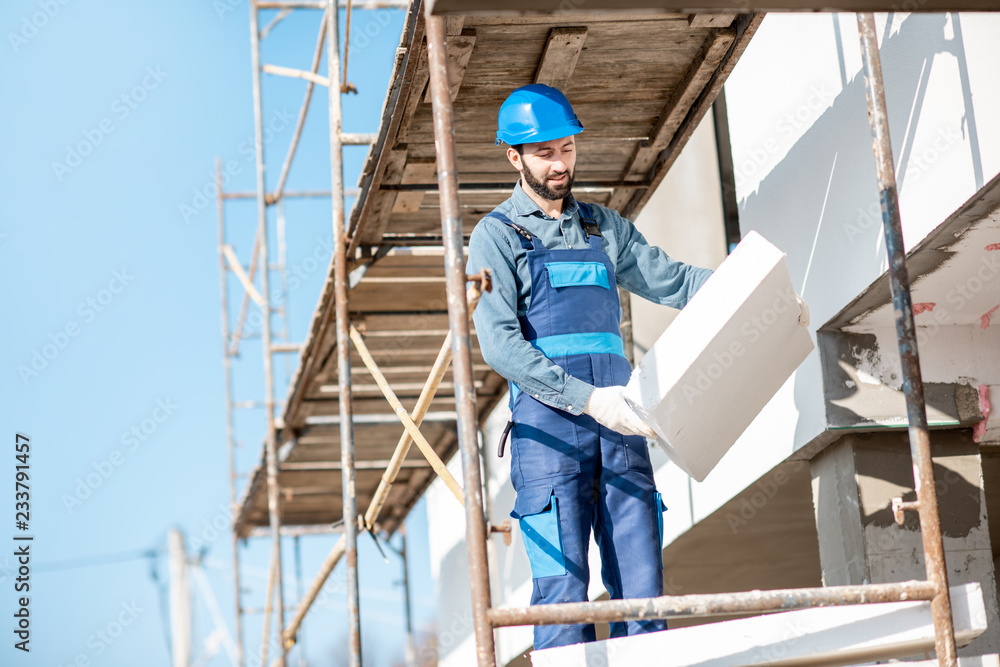 建筑工人用站在建筑脚手架上的泡沫板温暖建筑立面