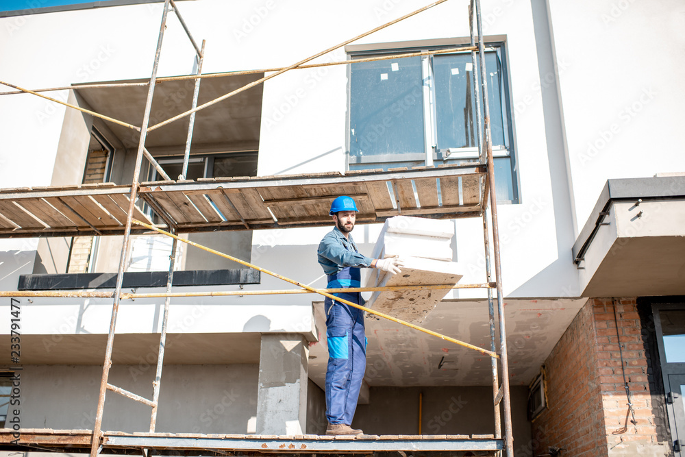 建筑工人用站在建筑脚手架上的泡沫板温暖建筑立面