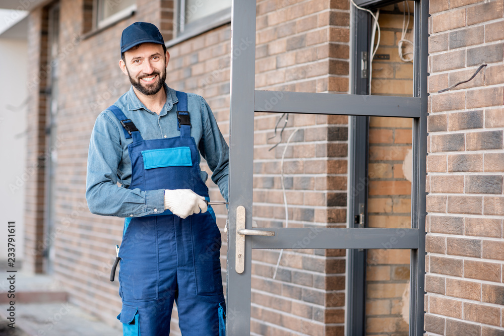 穿着制服的建筑工人在室外新房子的入口门上安装门锁