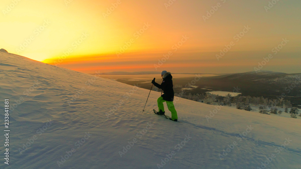 航空航天：活跃的女性雪鞋在冬季日出时在雪山斜坡上徒步旅行