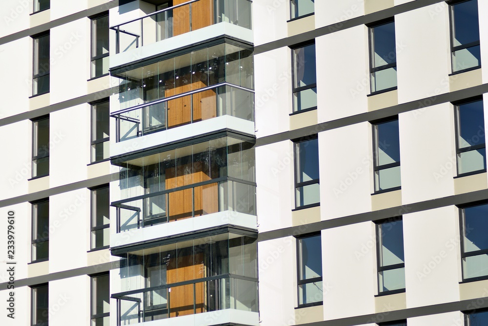  Fragment of a facade of a building with windows and balconies. Modern home with many flats.