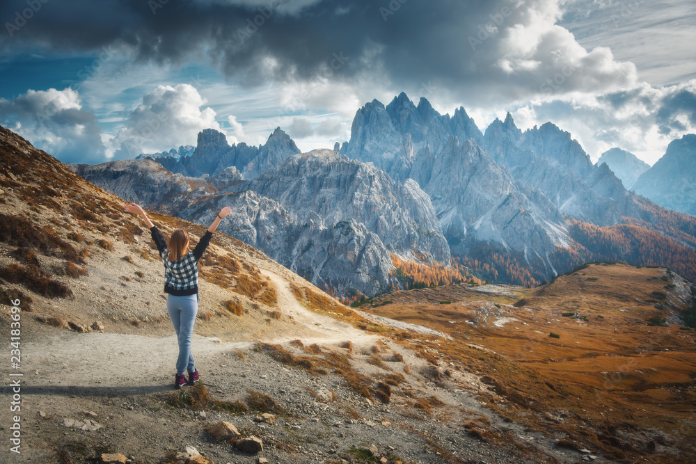 Young woman with raised up arms and majestic mountains at sunset in autumn in Dolomites, Italy. Land