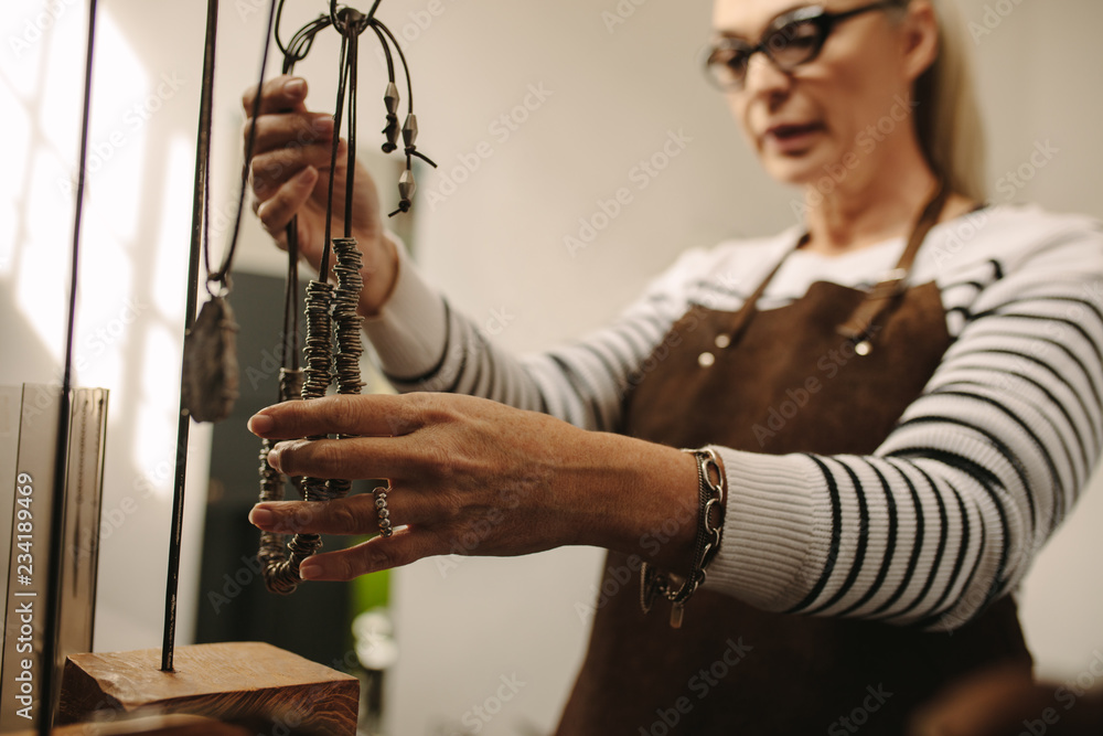 Mature female jeweler hanging a necklace on stand