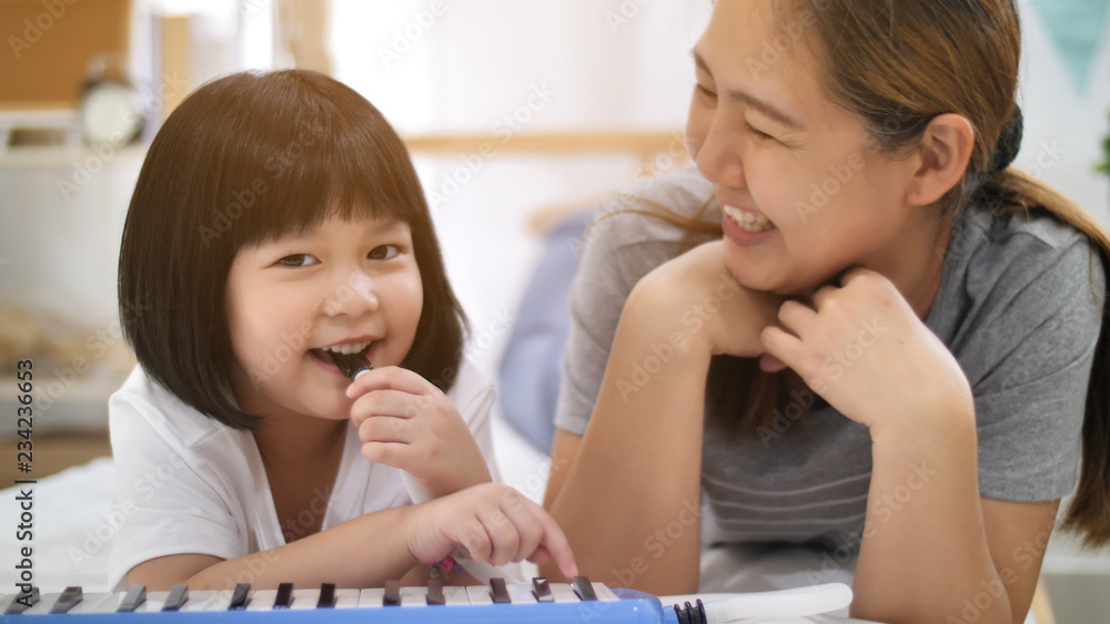 快乐的亚洲小女孩和妈妈一起演奏旋律吹风琴