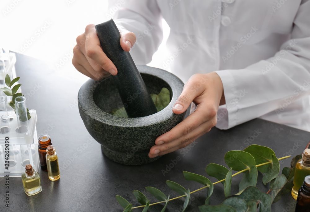 Pharmacologist pounding eucalyptus leaves in mortar on table