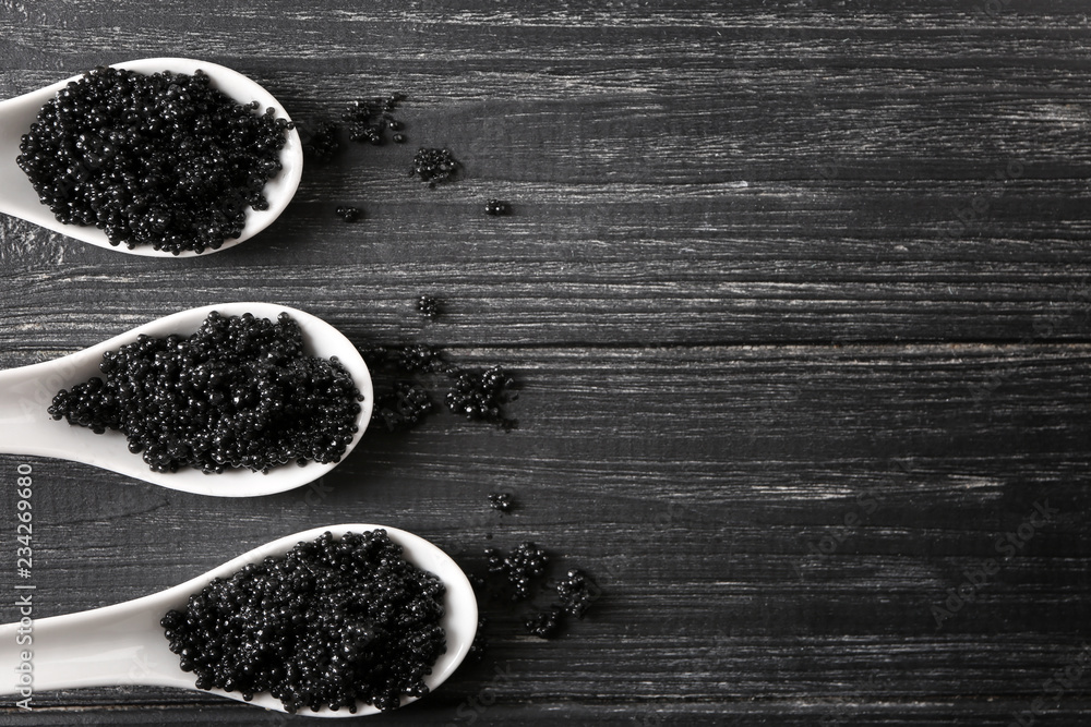 Spoons with delicious black caviar on wooden background