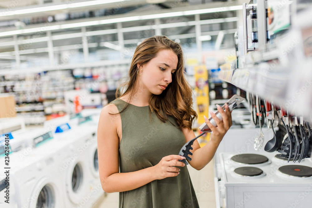 Woman shopping for diverse kitchen accessories in supermarket.