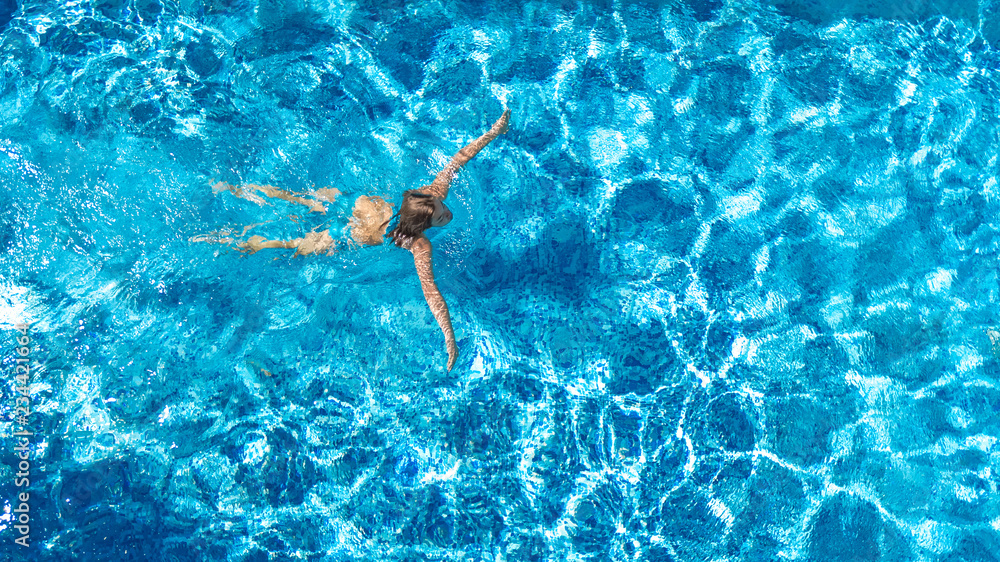 Active girl in swimming pool aerial drone view from above, young woman swims in blue water, tropical