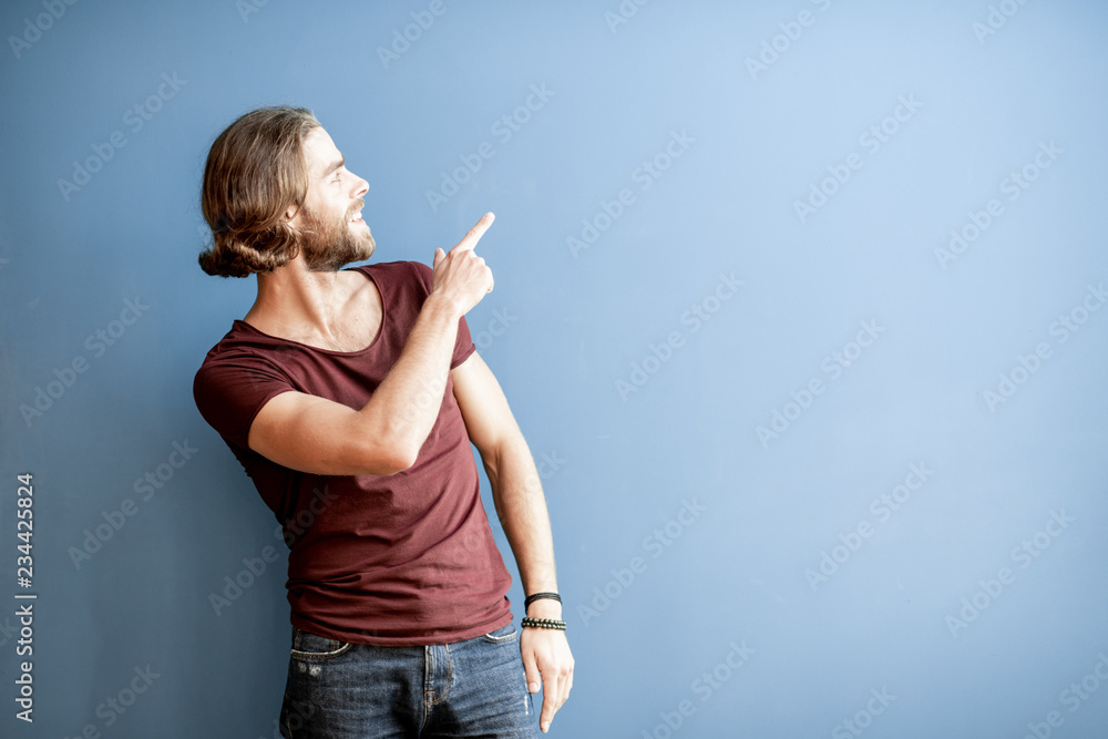 Portrait of a young caucasian bearded man with long hair dressed in t-shirt showing with hand on the