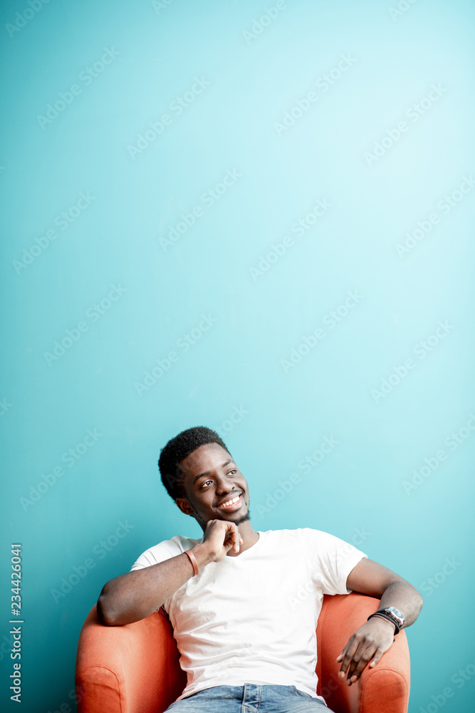 Portrait of a young african man dressed in white t-shirt and jeans sitting on the chair on the color