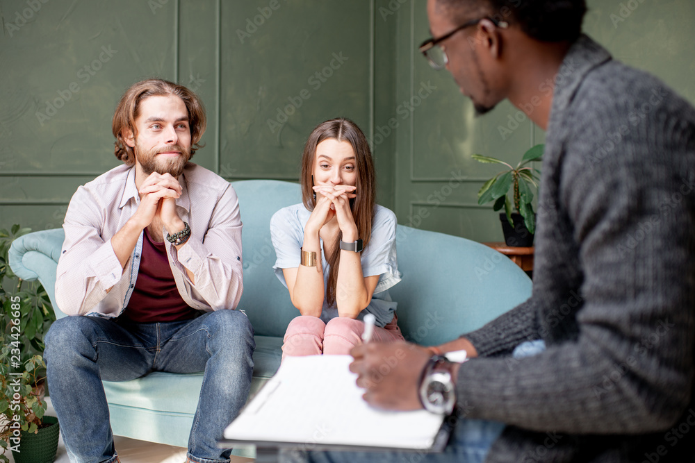 Young serious couple visiting a psychologist sitting on the comfortable couch during psychological s