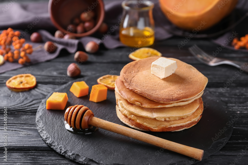 Stack of hot tasty pancakes with butter and pumpkin pieces on slate plate