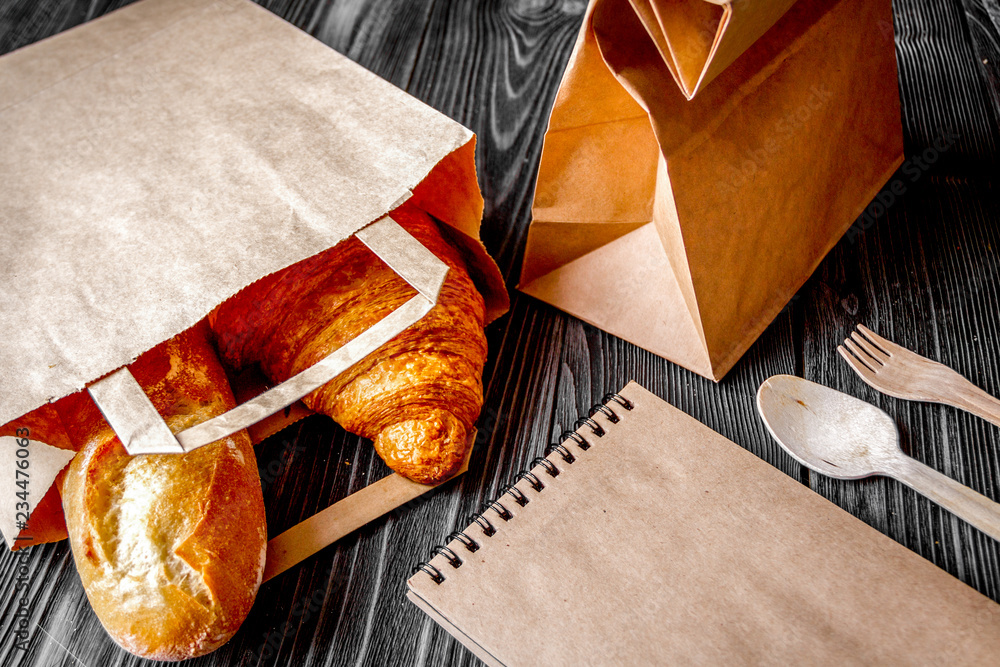 cup coffee and croissant in paper bag on wooden background