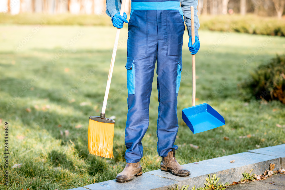 Sweeper in uniform with cleaning tools in the garden, cropped image with no face