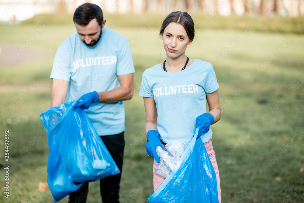 Portrait of a disappointed volunteers in blue t-shirts removing plastic rubbish in the park