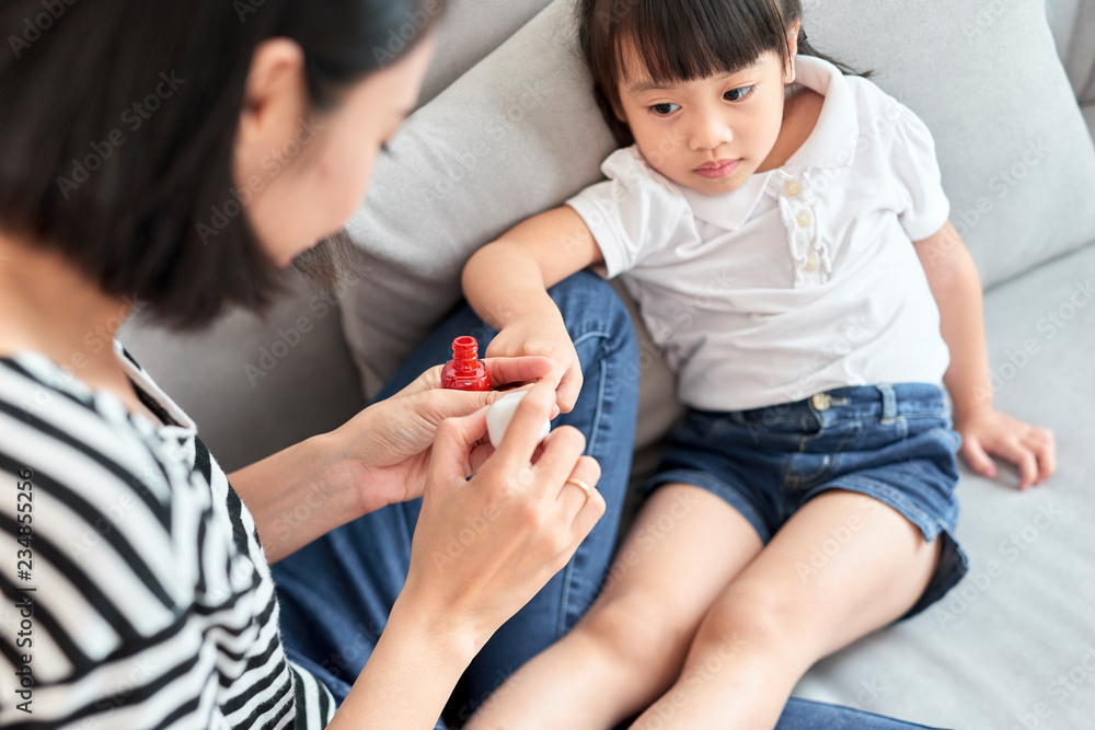 美丽的年轻妈妈正在给她可爱的小女儿涂指甲油