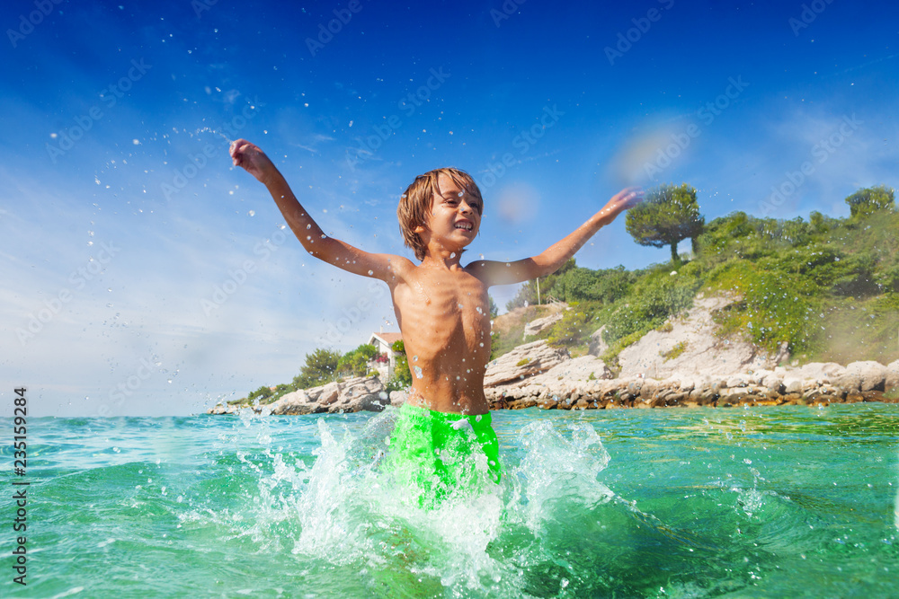 Cute boy having fun splashing water at the seaside