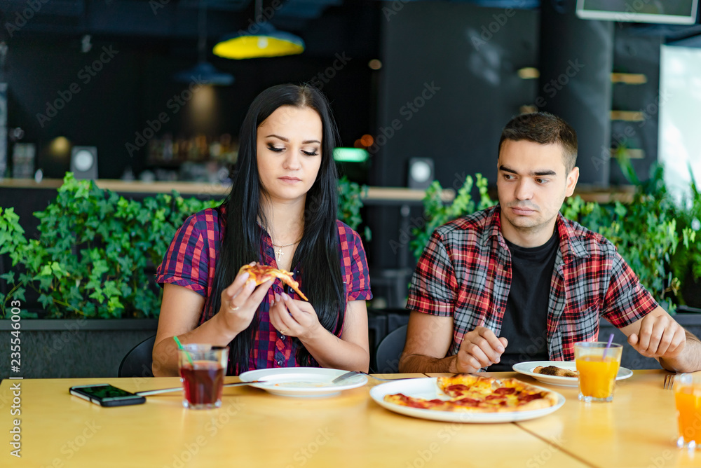 一对年轻夫妇在餐厅的背景上吃披萨。一个漂亮女孩和她的男朋友在检查