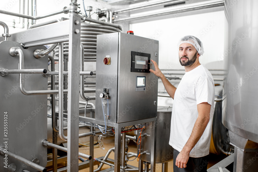 Worker operating pasteurizer using the control panel at the cheese or milk manufacturing